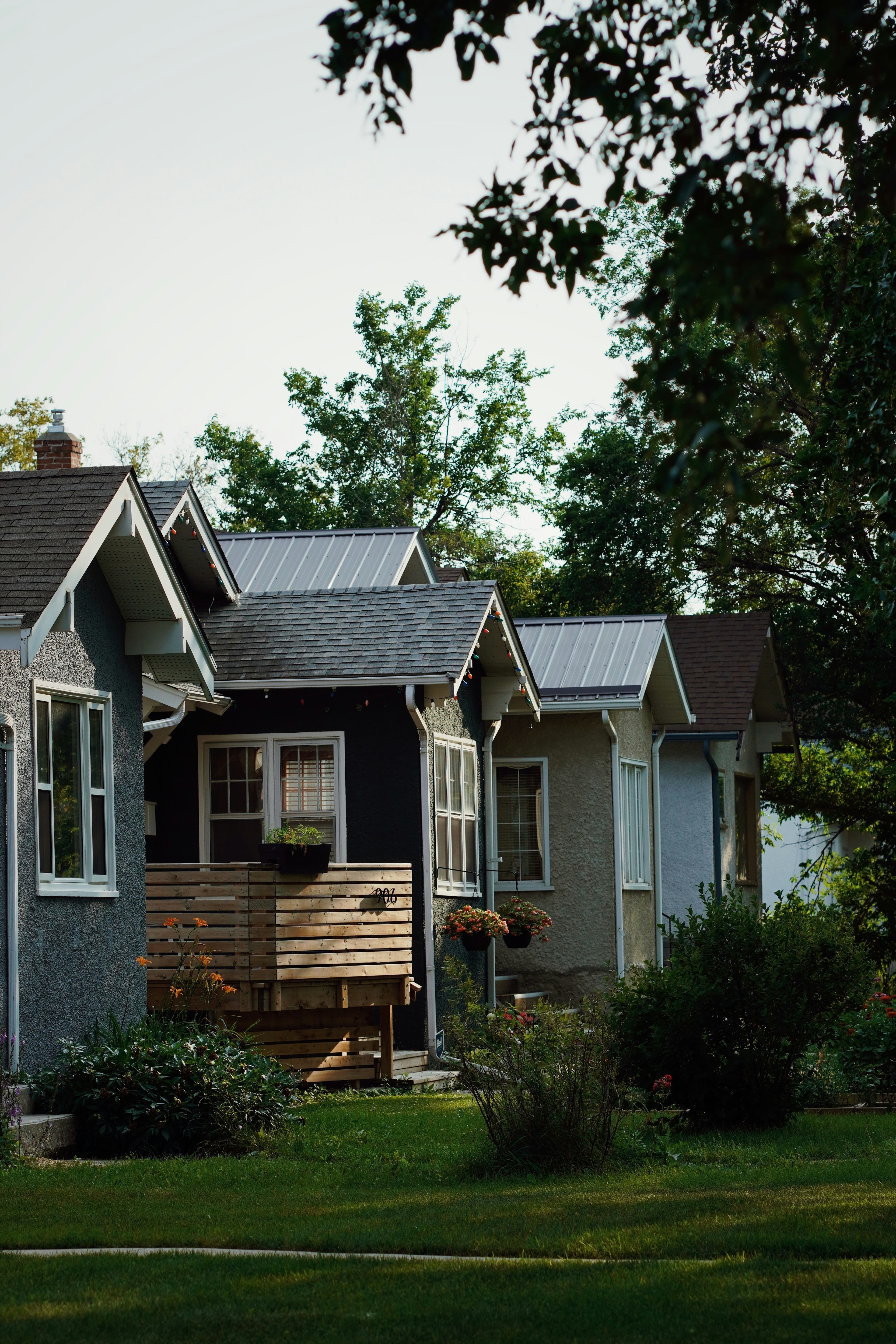 A row of modest single-story bungalows along a residential street, with green front lawns and flowering planters.